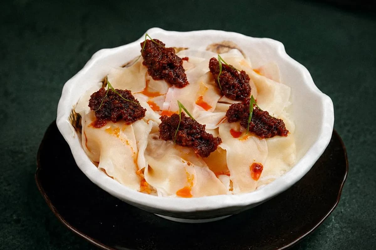 Folded dumplings topped with dark chili paste, in a white bowl on a dark plate.