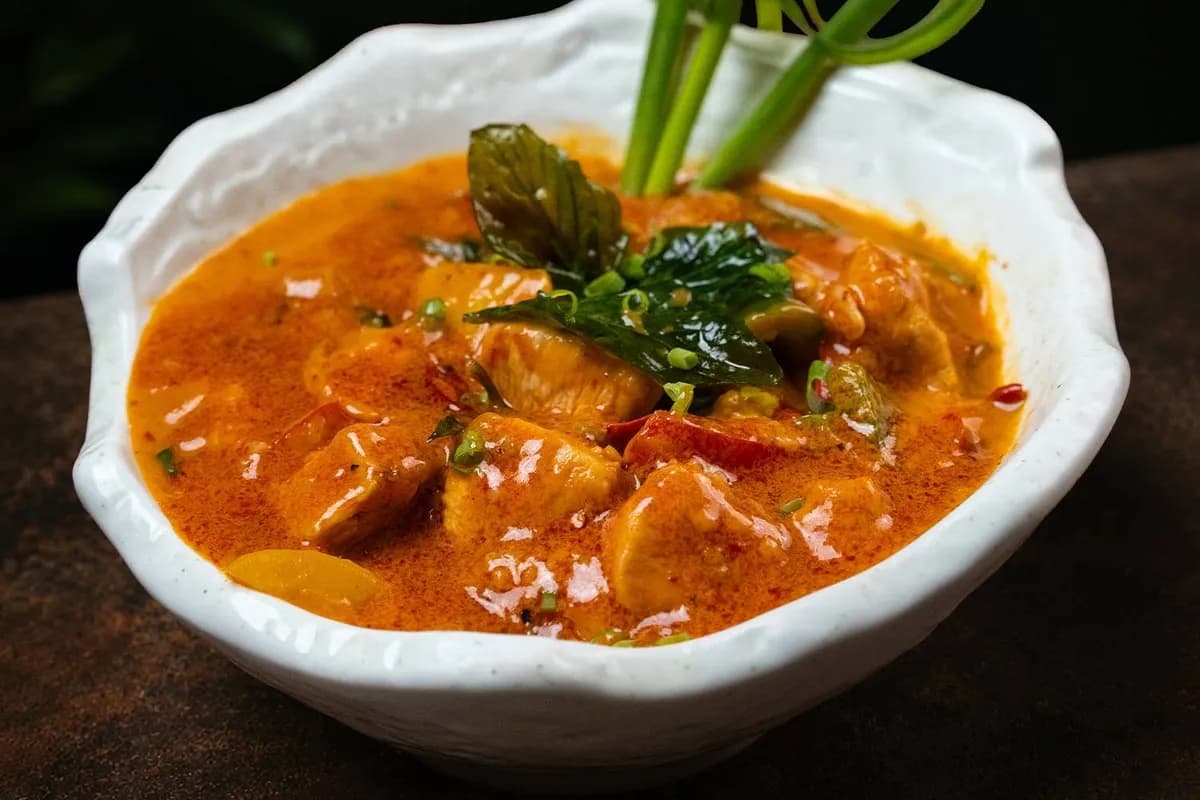 An orange curry topped with basil leaves, in a white bowl.