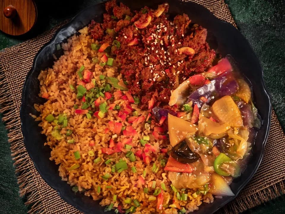 Fried rice, spiced beef with sesame and saucy vegetables on a dark plate, seen from above.