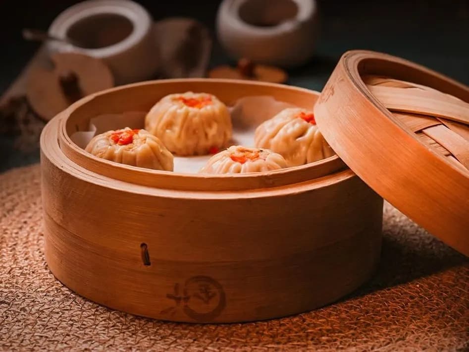 Sui mai dumplings in a bamboo steamer, its lid resting against the side.