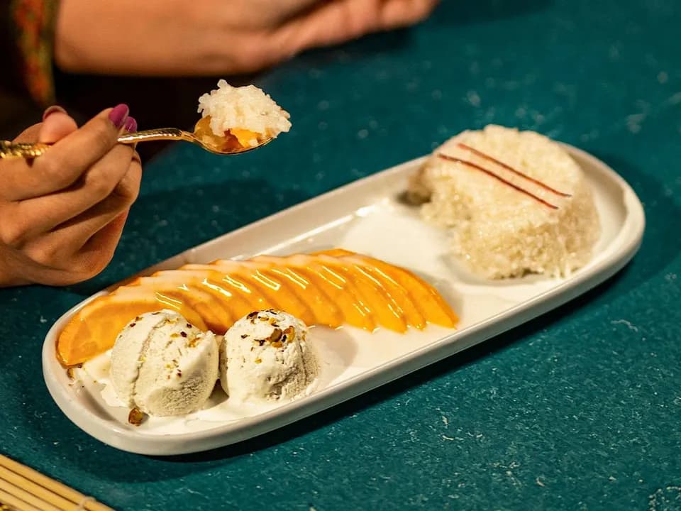 Sliced mango, two scoops of coconut ice cream and sticky rice on a long white dish.
