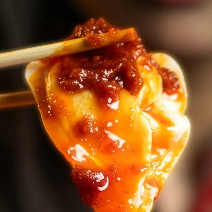 A dumpling coated in chili oil, lifted with chopsticks.