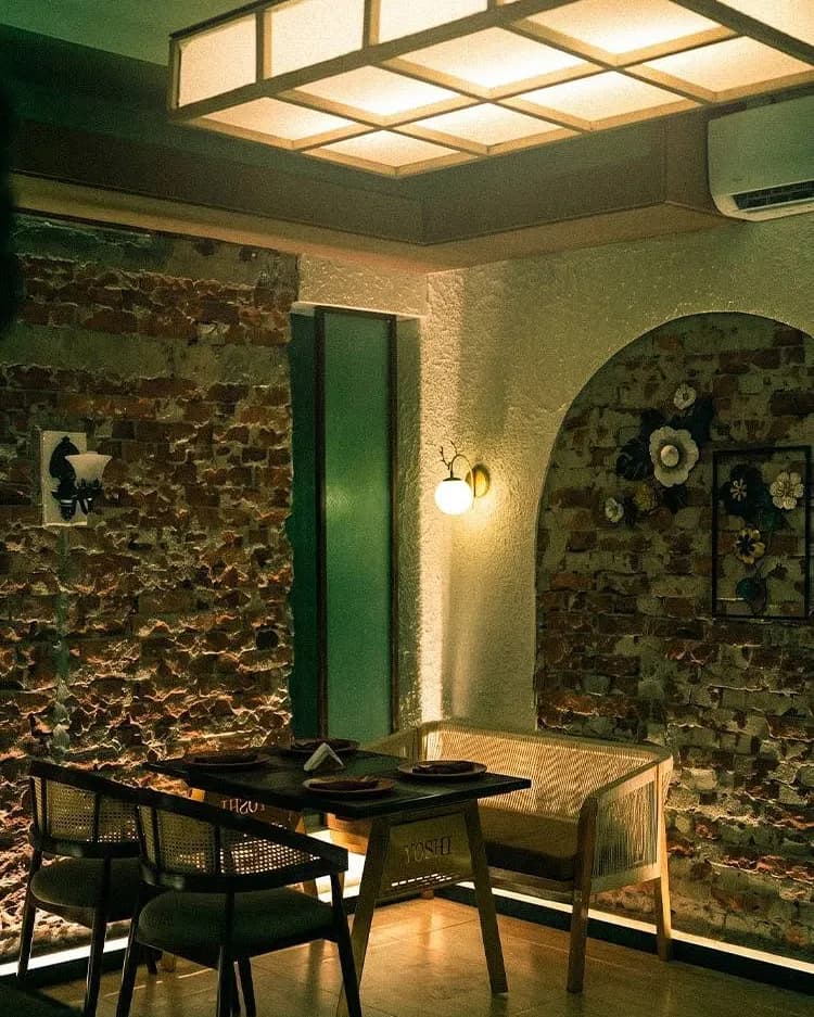 A table for four under a lattice ceiling light, beside an arched alcove and a brick wall.