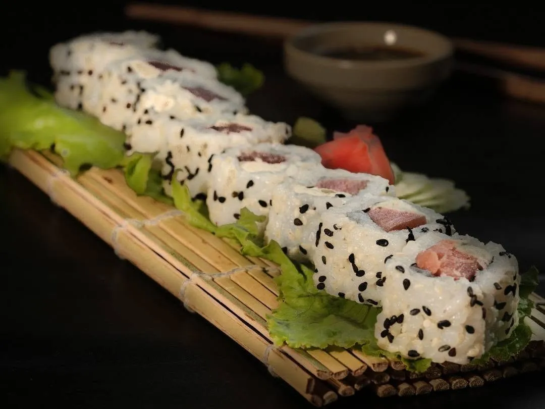 Rice-outside rolls with tuna, dotted with black sesame, on lettuce and a bamboo mat.