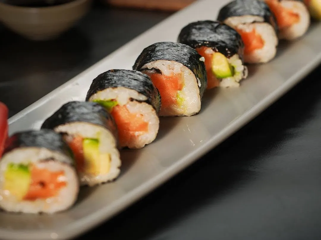A row of nori-wrapped rolls filled with salmon and avocado on a long grey plate.